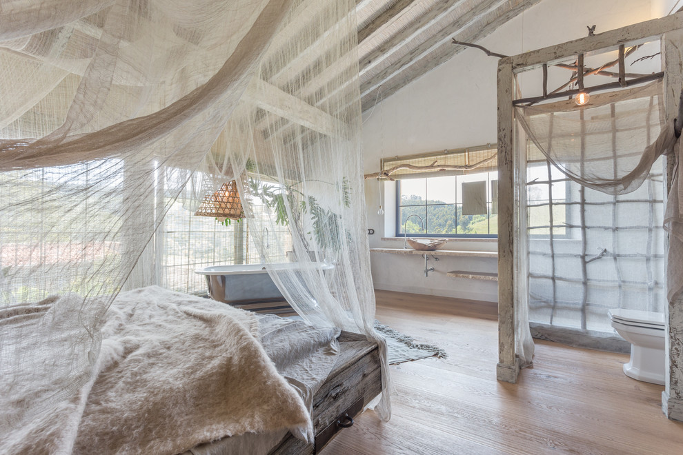 Modelo de dormitorio principal campestre grande sin chimenea con paredes blancas y suelo de madera clara