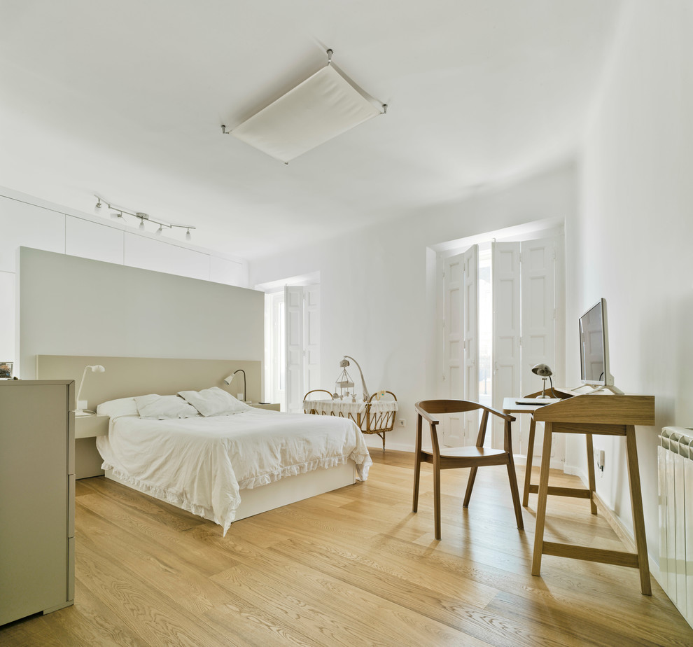 Modelo de dormitorio principal actual grande sin chimenea con paredes blancas, suelo de madera en tonos medios y con escritorio