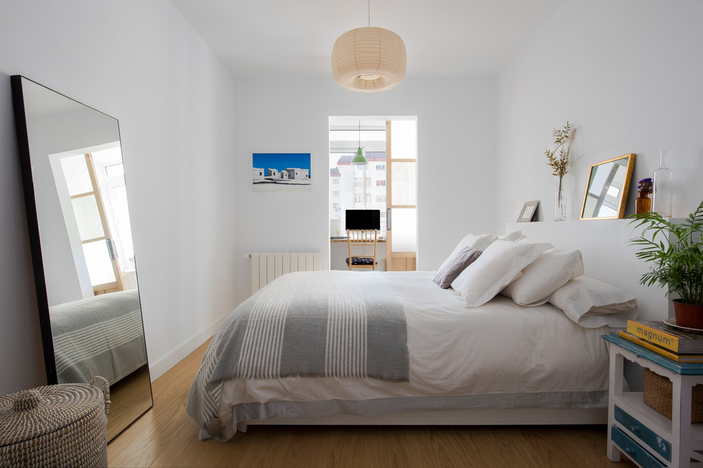 Imagen de dormitorio principal nórdico de tamaño medio sin chimenea con paredes blancas, suelo de madera en tonos medios y suelo marrón
