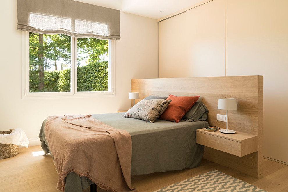 Modelo de dormitorio principal escandinavo de tamaño medio sin chimenea con paredes blancas, suelo de madera en tonos medios y suelo marrón
