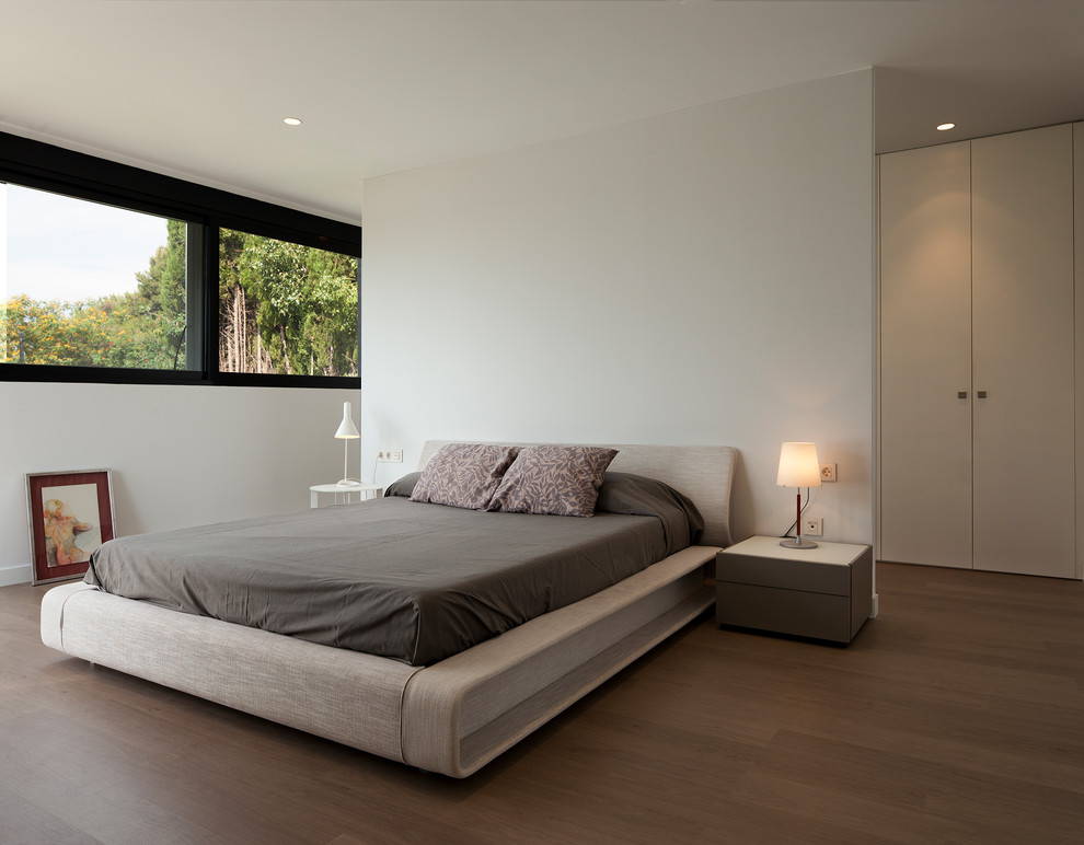 Modelo de dormitorio contemporáneo grande con paredes blancas, suelo de madera oscura y suelo marrón