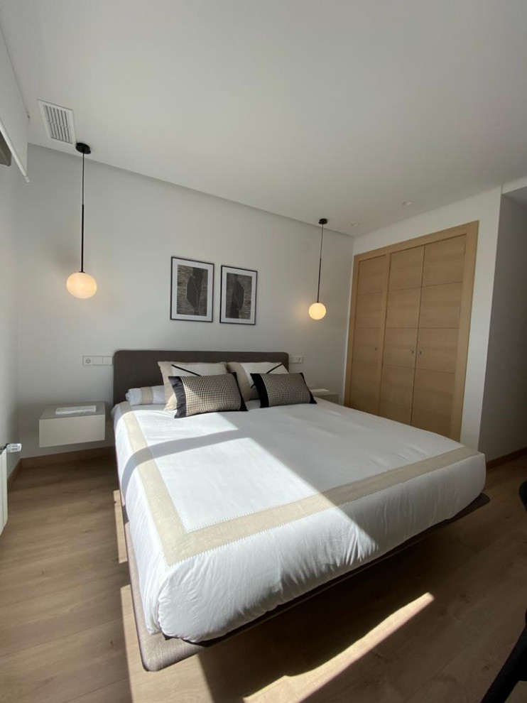 Modelo de dormitorio escandinavo con paredes blancas, suelo de madera clara y suelo marrón