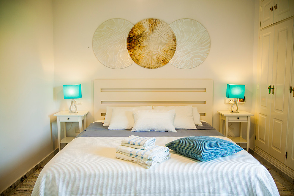 Ejemplo de dormitorio principal costero pequeño con paredes blancas, suelo de mármol y suelo gris