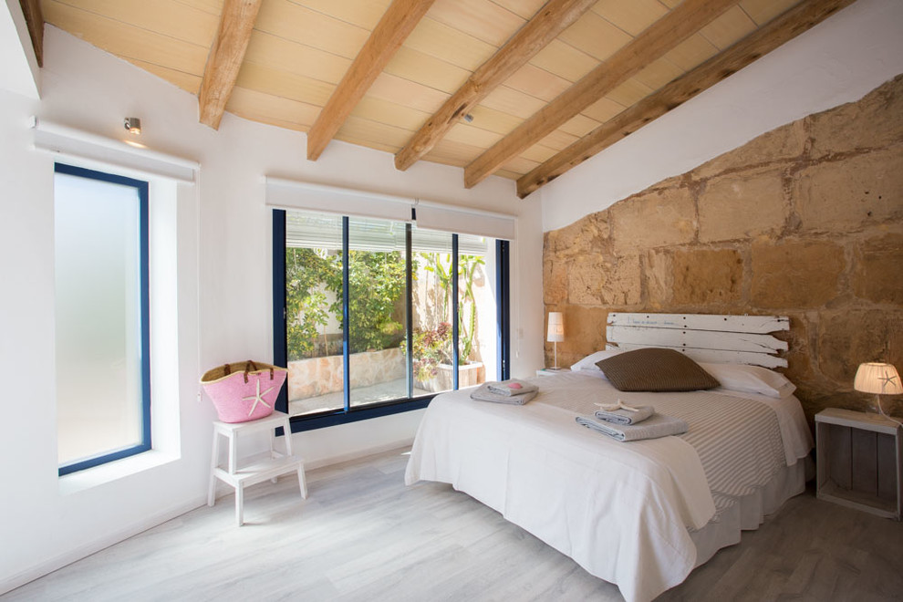 Modelo de dormitorio principal rural de tamaño medio sin chimenea con paredes blancas y suelo de madera clara