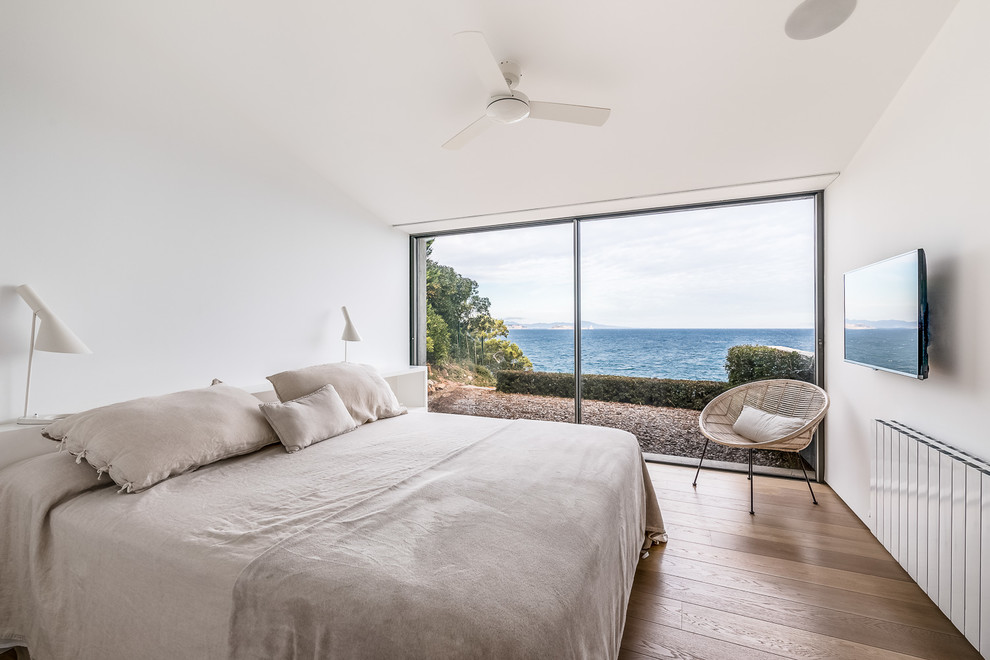 Maritimes Schlafzimmer mit weißer Wandfarbe, braunem Holzboden und braunem Boden in Sonstige
