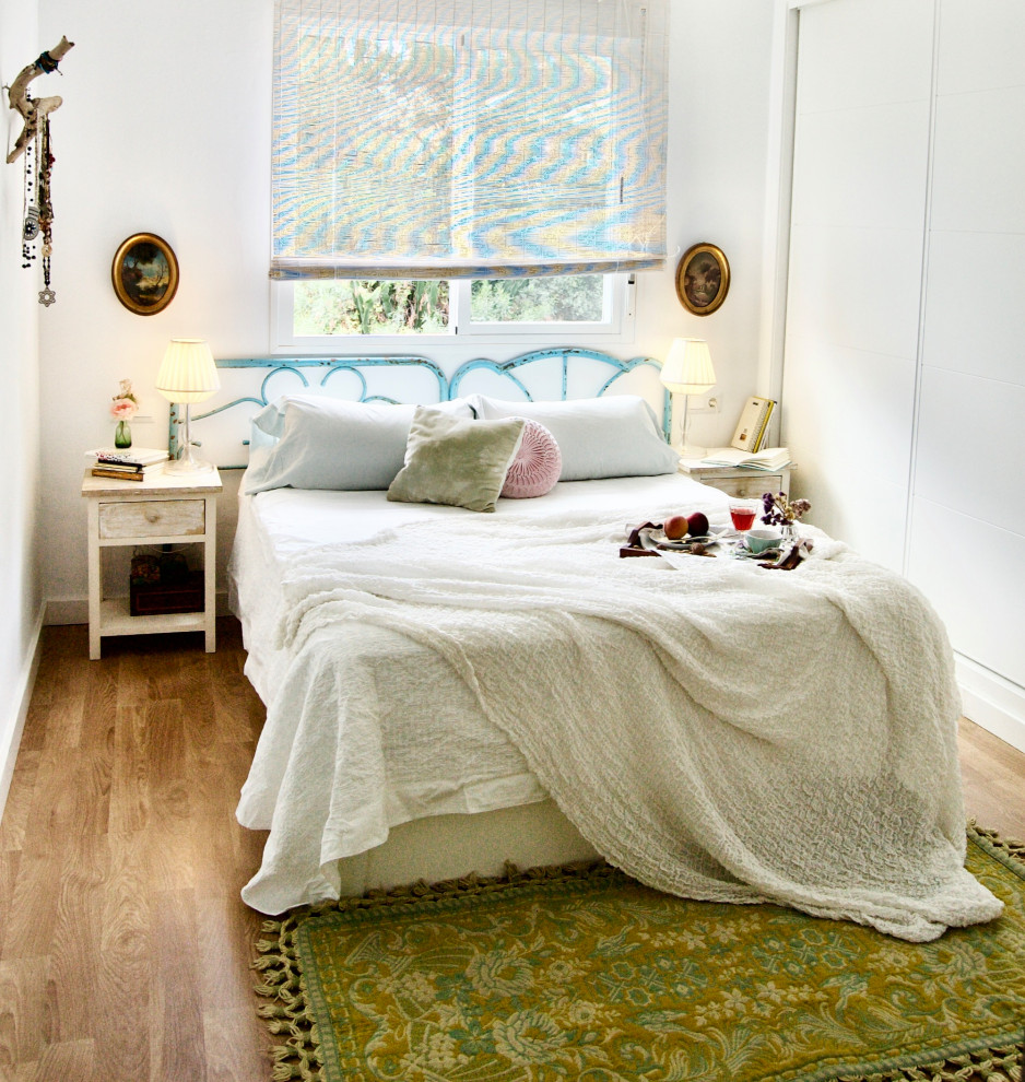 На фото: хозяйская спальня среднего размера в стиле фьюжн с белыми стенами, полом из ламината и коричневым полом с