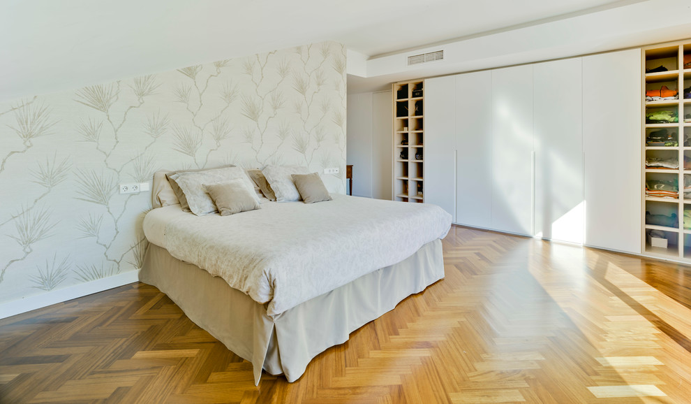 Modelo de dormitorio principal actual grande sin chimenea con paredes blancas y suelo de madera en tonos medios