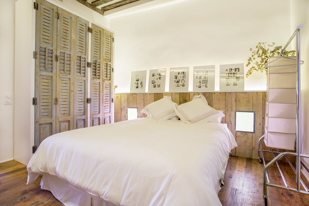 Immagine di una camera matrimoniale industriale di medie dimensioni con pareti bianche, pavimento in legno massello medio e nessun camino