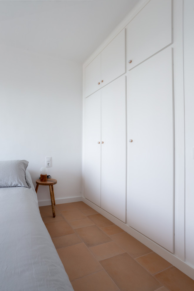 Imagen de dormitorio principal mediterráneo de tamaño medio sin chimenea con paredes blancas, suelo de baldosas de terracota y suelo marrón