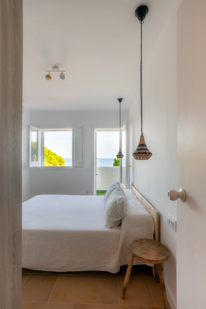 Modelo de dormitorio principal mediterráneo de tamaño medio sin chimenea con paredes blancas, suelo de baldosas de terracota y suelo marrón