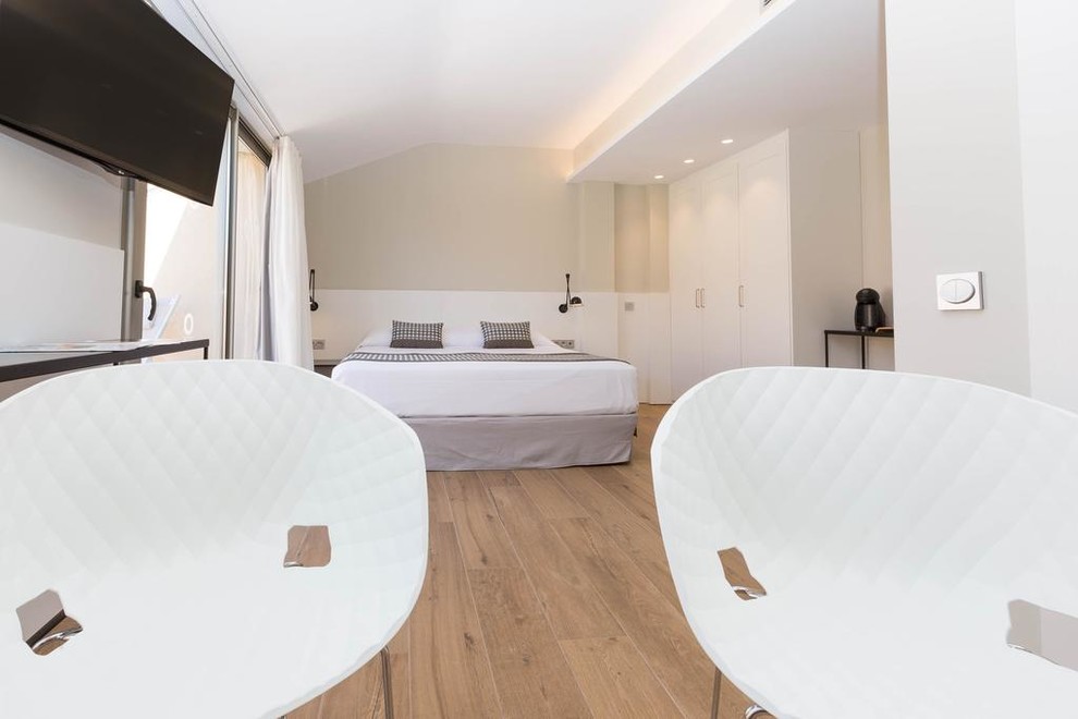 Modelo de dormitorio principal nórdico pequeño con paredes blancas, suelo de madera en tonos medios y suelo marrón