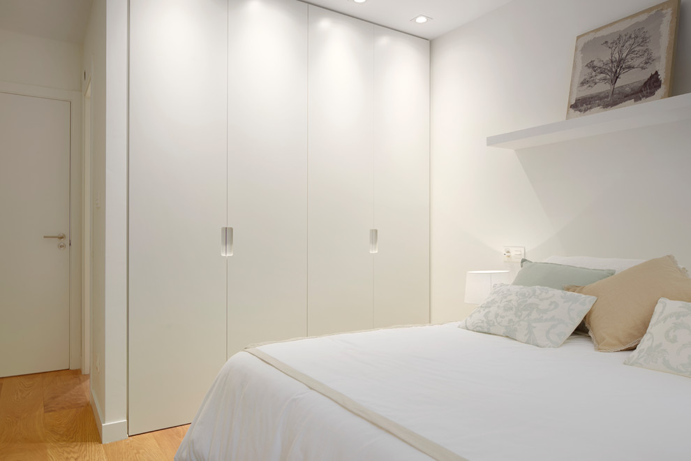 Ejemplo de dormitorio principal clásico renovado de tamaño medio sin chimenea con paredes blancas, suelo de madera en tonos medios y suelo marrón