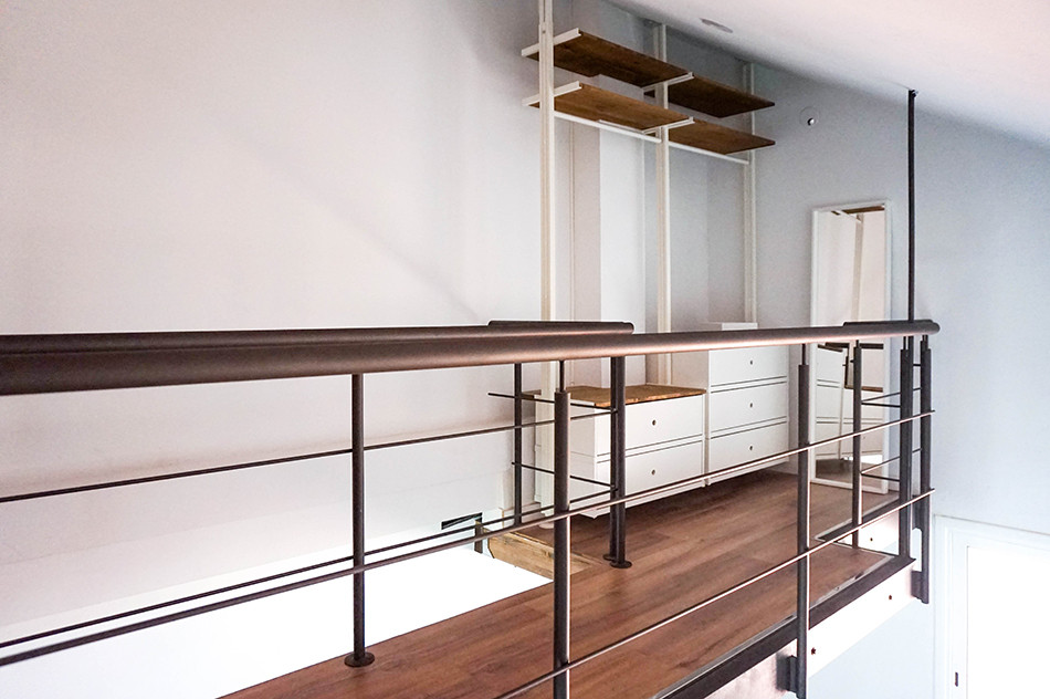 Ejemplo de dormitorio tipo loft industrial de tamaño medio con paredes blancas, suelo laminado y suelo marrón