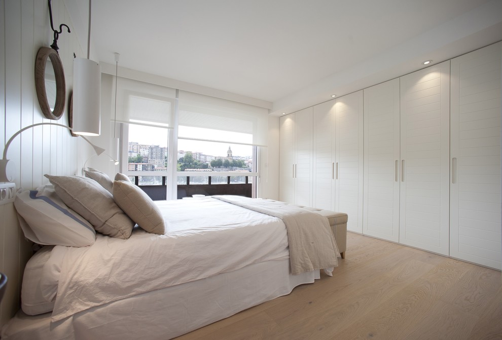 Ejemplo de dormitorio principal costero grande con paredes blancas, suelo de madera clara y suelo marrón