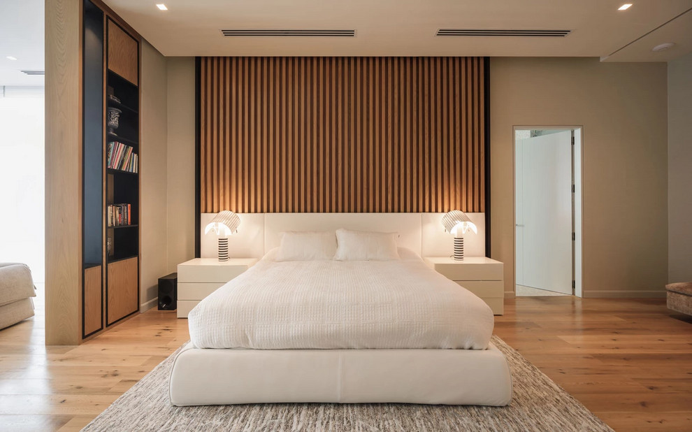 Large modern master bedroom in Barcelona with beige walls, medium hardwood flooring and brown floors.