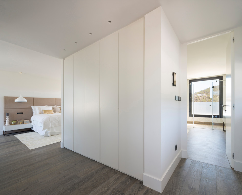 Immagine di una grande camera matrimoniale minimal con pareti bianche, pavimento in legno massello medio e pavimento marrone