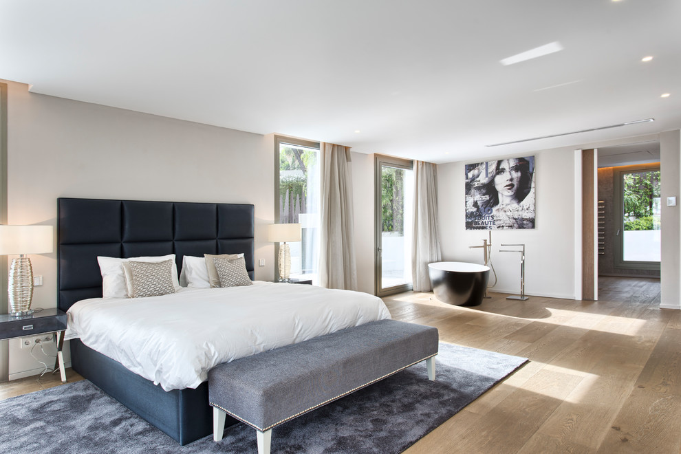 Modelo de dormitorio actual grande con paredes grises, suelo de madera en tonos medios y suelo marrón