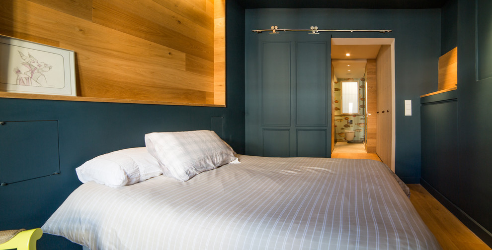 Modelo de dormitorio principal actual de tamaño medio con paredes azules, suelo de madera en tonos medios y suelo marrón
