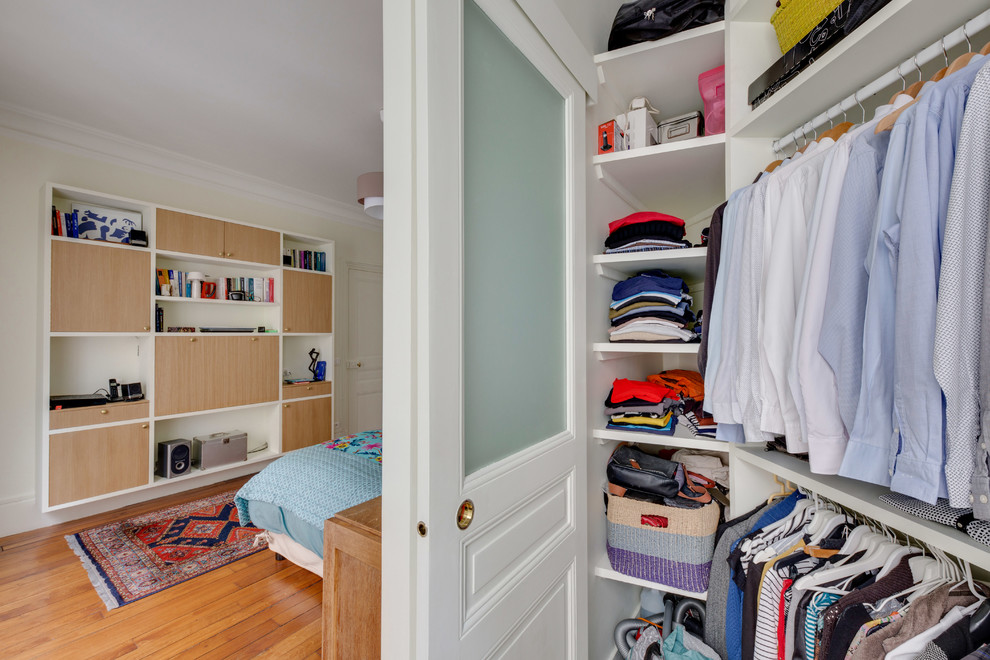 This is an example of a medium sized contemporary gender neutral walk-in wardrobe in Paris with beaded cabinets, white cabinets, dark hardwood flooring and brown floors.