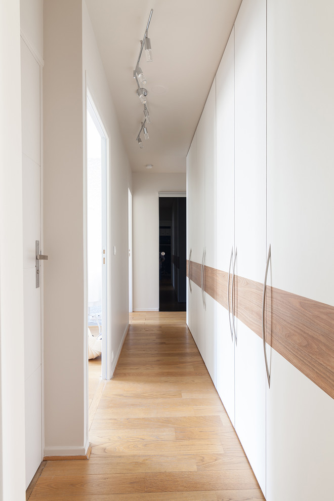 Exempel på ett stort modernt walk-in-closet för könsneutrala, med luckor med profilerade fronter, vita skåp, ljust trägolv och brunt golv
