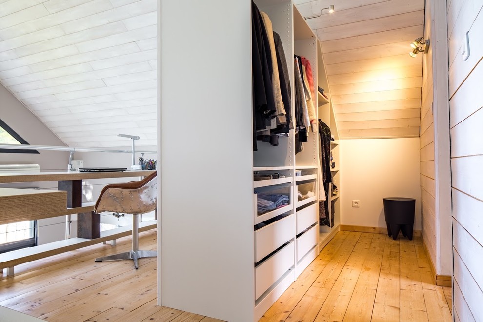 Cette image montre un dressing room design neutre avec un placard à porte plane, des portes de placard blanches et un sol en bois clair.