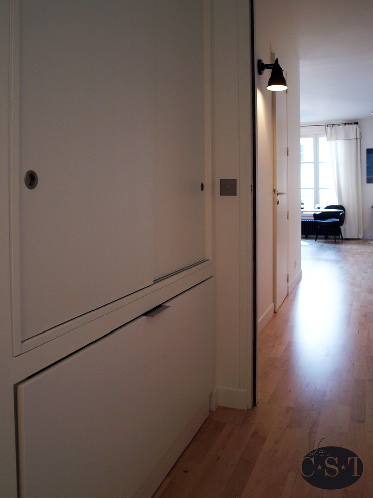 This is an example of a small contemporary gender neutral standard wardrobe in Paris with white cabinets and light hardwood flooring.