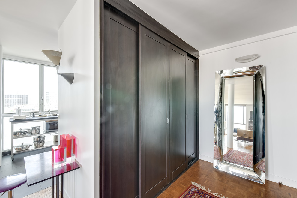 This is an example of a medium sized contemporary gender neutral standard wardrobe in Paris with light hardwood flooring, brown floors, recessed-panel cabinets and dark wood cabinets.