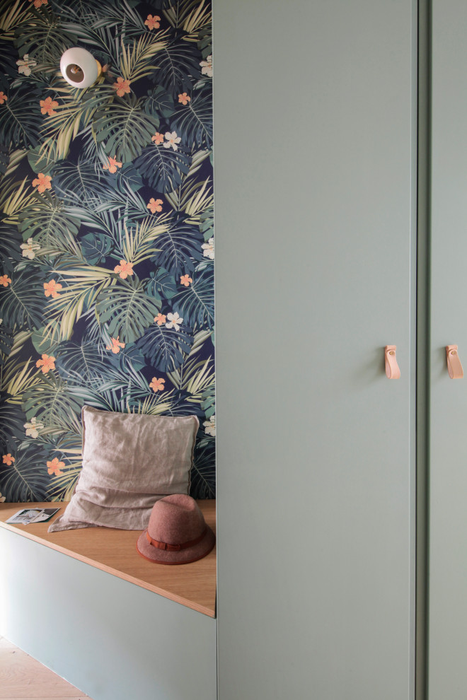 Large scandi gender neutral walk-in wardrobe in Paris with green cabinets and light hardwood flooring.