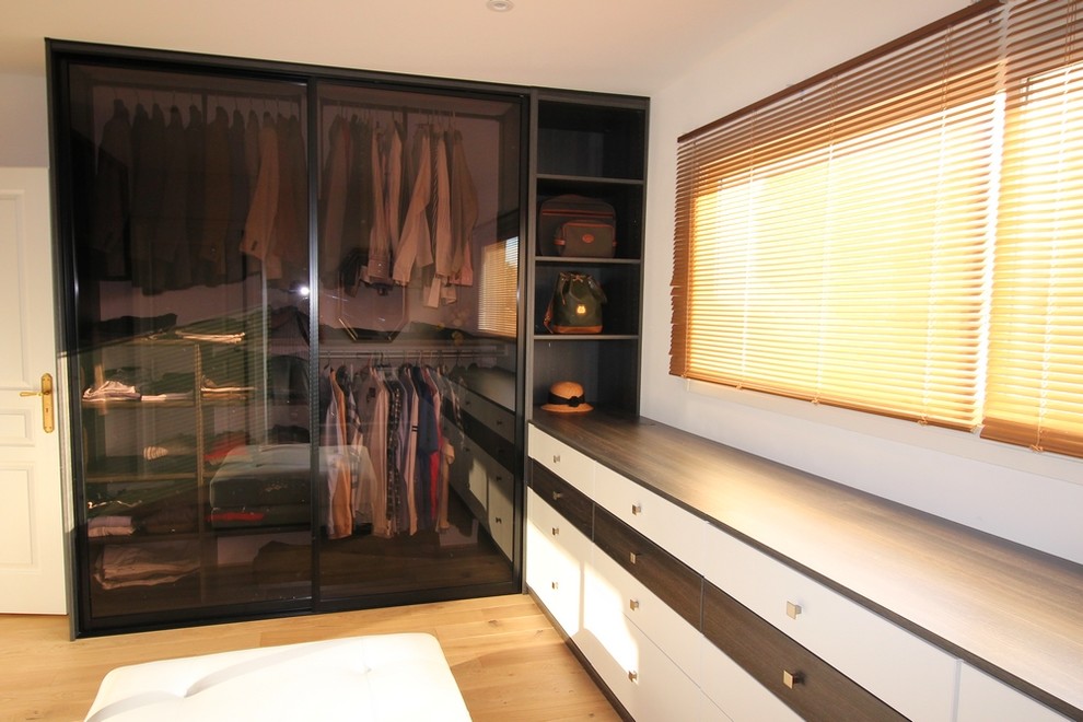 Cette photo montre un grand dressing tendance en bois foncé neutre avec un placard à porte vitrée, parquet clair et un sol beige.