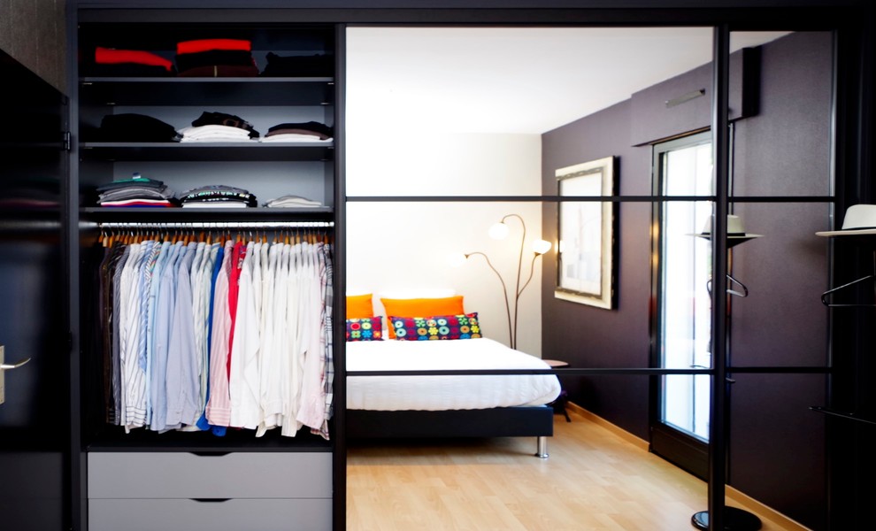 Diseño de armario unisex actual de tamaño medio con puertas de armario negras y suelo de madera clara