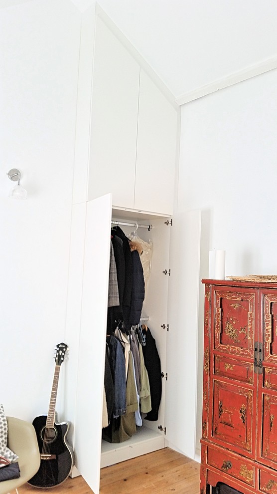 Cette photo montre un placard dressing tendance de taille moyenne et neutre avec un placard à porte affleurante, des portes de placard blanches et parquet clair.