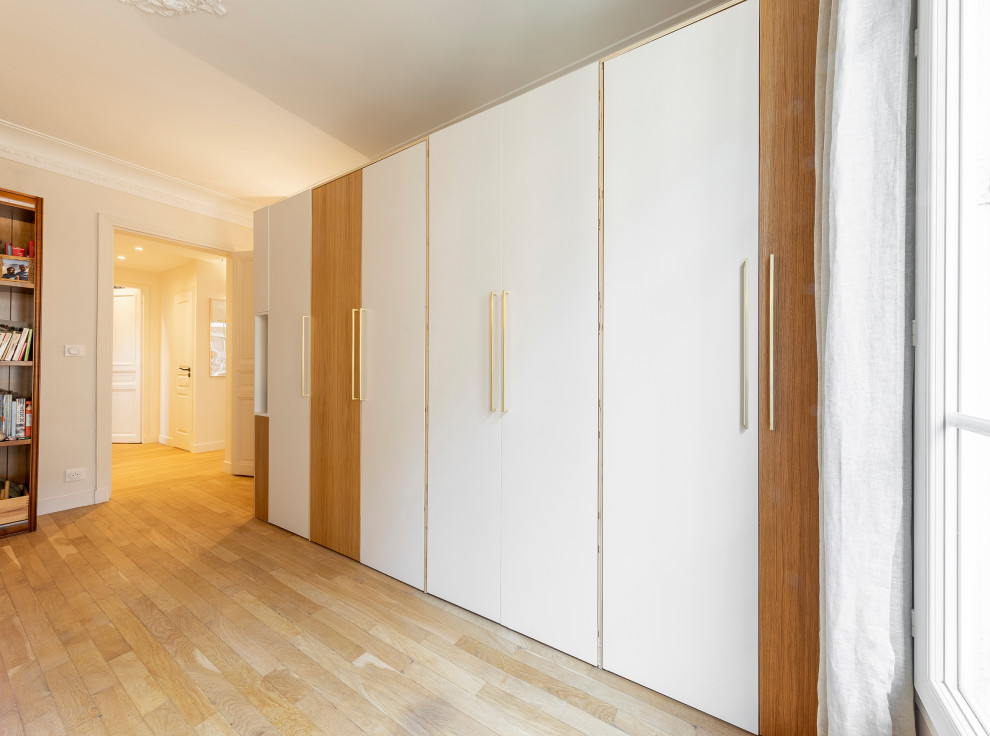 Diseño de armario unisex actual de tamaño medio con armarios con rebordes decorativos, puertas de armario de madera clara, suelo de madera clara y suelo beige