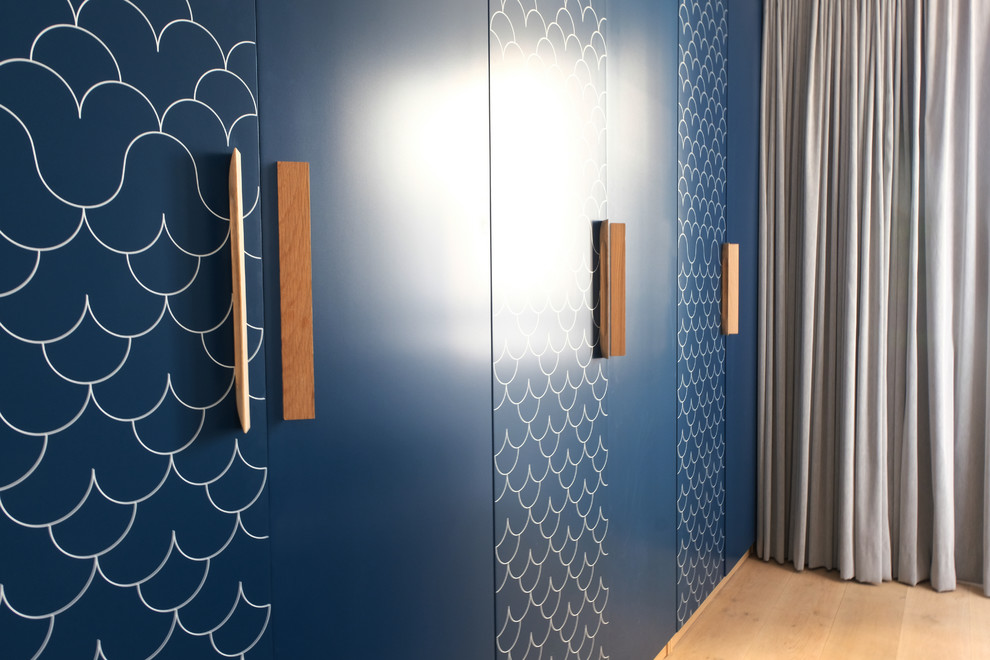 Cette image montre un placard dressing design avec des portes de placard bleues et parquet clair.