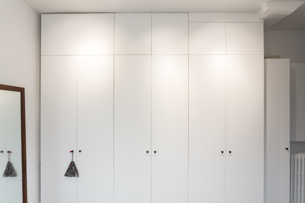 Cette image montre un placard dressing minimaliste neutre et de taille moyenne avec un placard à porte affleurante et des portes de placard blanches.
