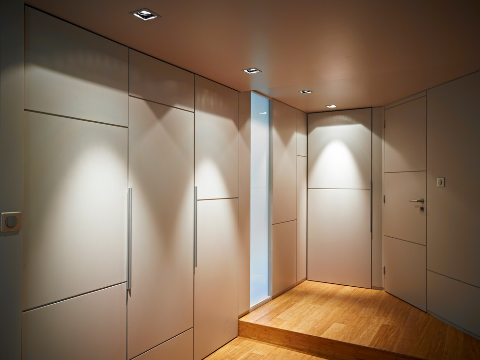 Ejemplo de vestidor unisex contemporáneo de tamaño medio con puertas de armario beige, suelo de bambú y armarios con paneles lisos
