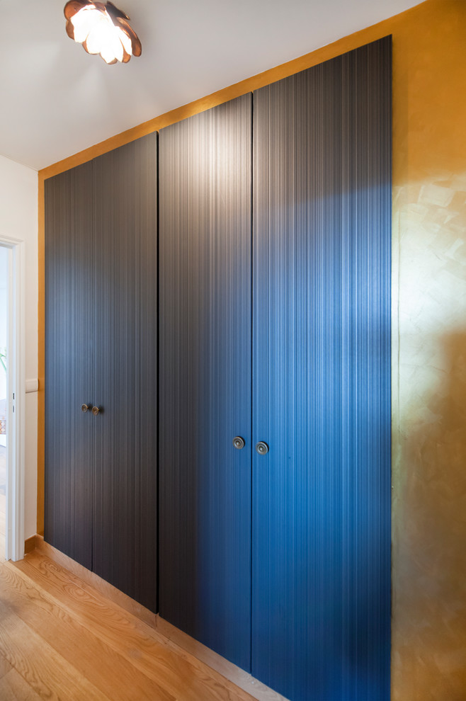 Example of a mid-sized trendy gender-neutral medium tone wood floor and beige floor reach-in closet design in Paris with blue cabinets