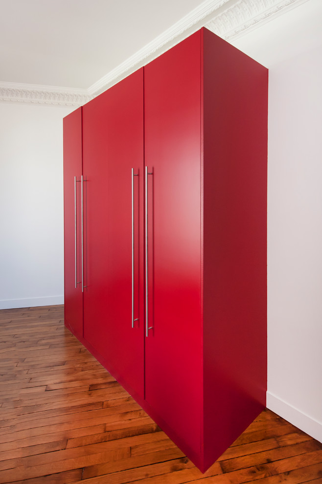 Photo of a large contemporary gender neutral standard wardrobe in Paris with red cabinets, medium hardwood flooring and beige floors.
