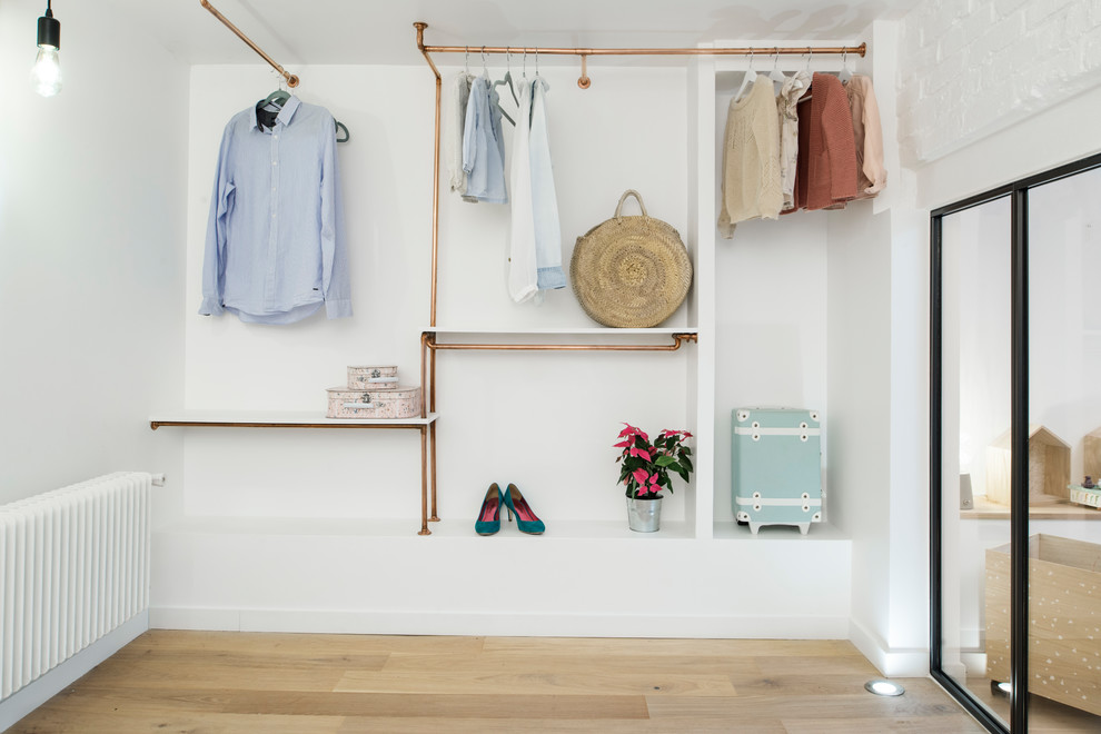 Réalisation d'un grand dressing nordique pour une femme avec un sol en bois clair, un placard sans porte et un sol beige.