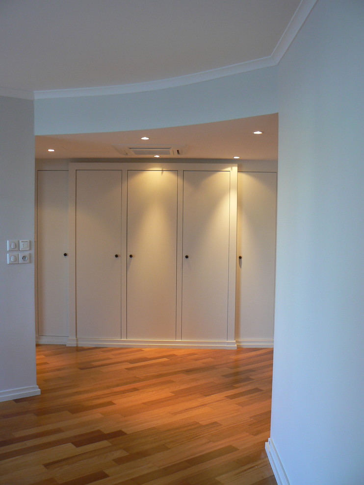 Cette image montre un grand placard dressing design neutre avec des portes de placard blanches et un sol en bois brun.