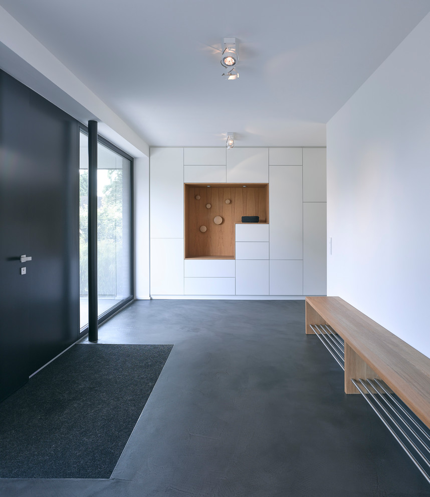 Пример оригинального дизайна: большое фойе: освещение в скандинавском стиле с белыми стенами, бетонным полом, одностворчатой входной дверью, черной входной дверью и серым полом