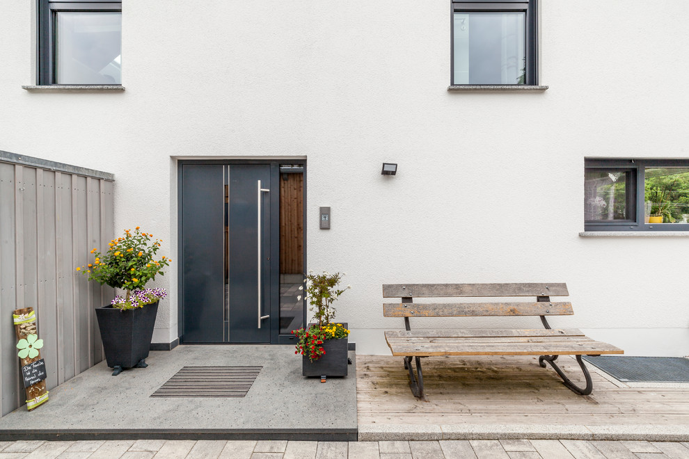 Cette image montre une porte d'entrée design de taille moyenne avec un mur blanc, sol en béton ciré, une porte simple, une porte noire et un sol gris.