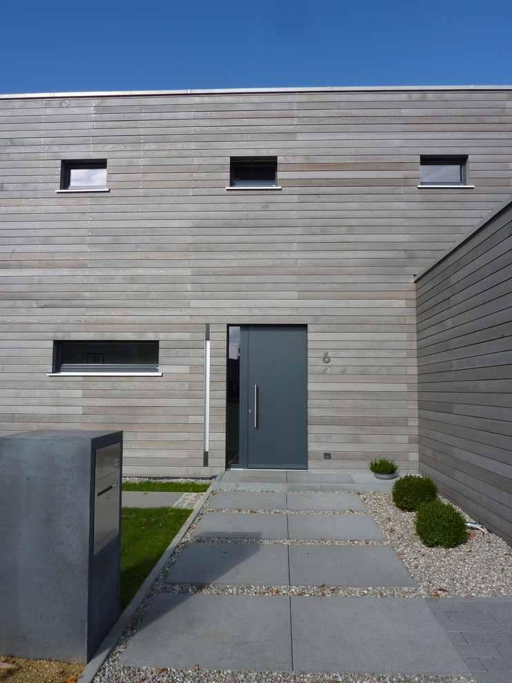Cette image montre une porte d'entrée minimaliste de taille moyenne avec un mur marron, sol en béton ciré, une porte simple, une porte grise et un sol gris.