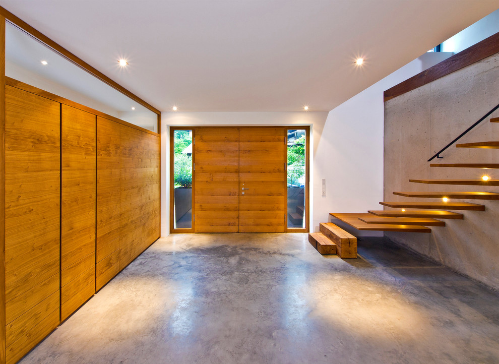 Ispirazione per un ingresso design con pareti bianche, pavimento in cemento, una porta a due ante, una porta marrone e pavimento grigio