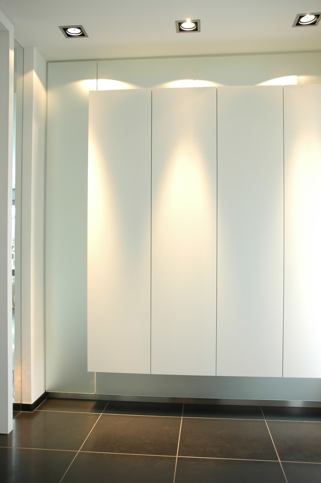 Cette image montre un grand hall d'entrée minimaliste avec un mur blanc, un sol en carrelage de porcelaine, une porte double, une porte blanche et un sol noir.