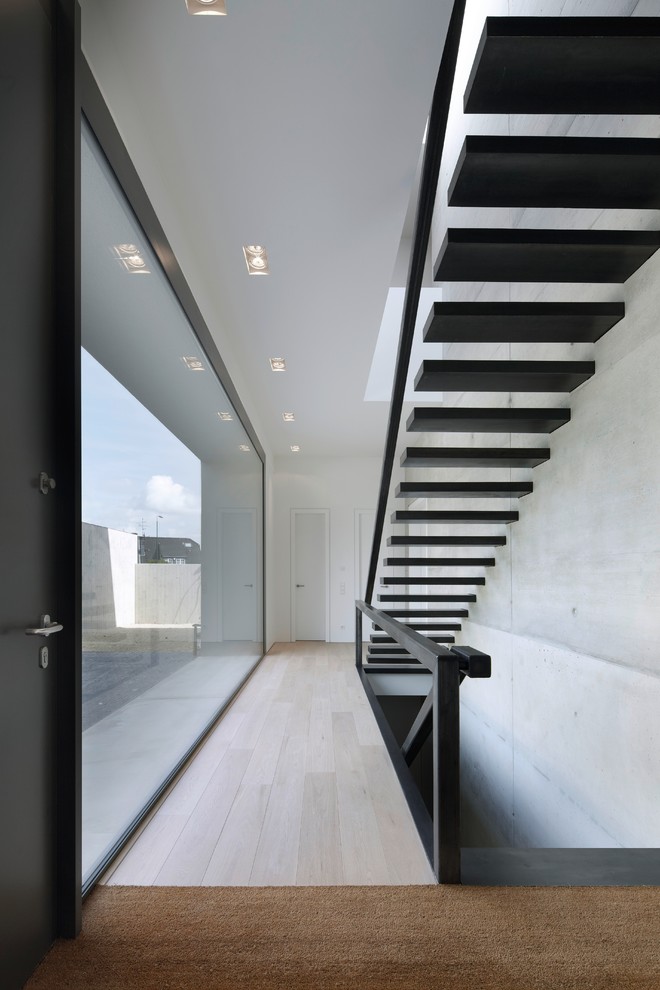 Idée de décoration pour un grand hall d'entrée design avec un mur gris, parquet clair et une porte noire.