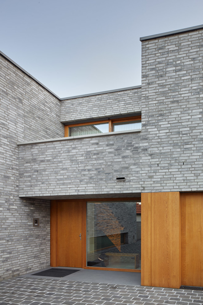 Imagen de puerta principal moderna de tamaño medio con paredes grises, suelo de granito, puerta simple, puerta de madera en tonos medios y suelo gris