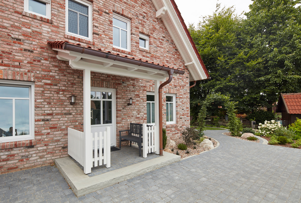 Réalisation d'une porte d'entrée champêtre de taille moyenne avec un mur rouge, une porte simple, une porte blanche et un sol gris.