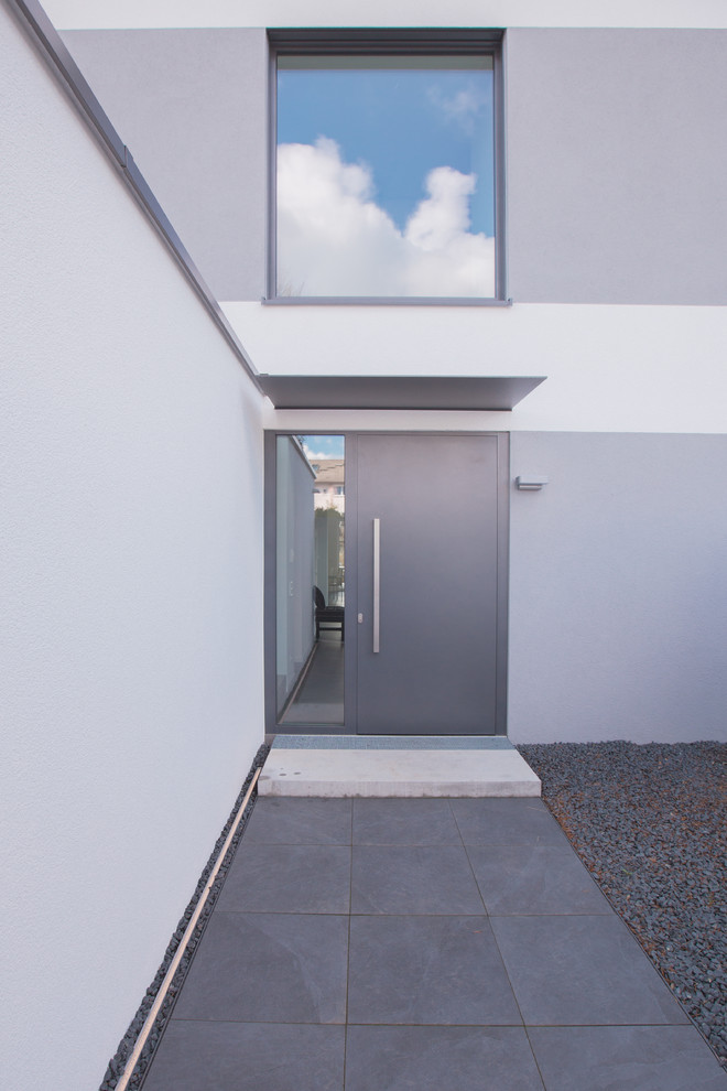 Cette photo montre une porte d'entrée tendance avec un mur blanc, un sol en ardoise, une porte double et une porte grise.