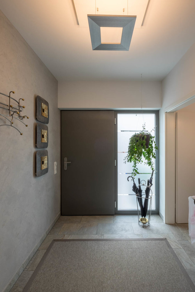 На фото: маленькая узкая прихожая в современном стиле с белыми стенами, полом из керамической плитки, черной входной дверью и серым полом для на участке и в саду с