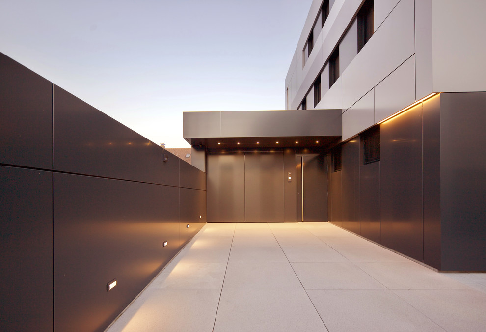 Aménagement d'une grande porte d'entrée contemporaine avec un mur noir, sol en béton ciré, une porte simple, une porte métallisée et un sol gris.